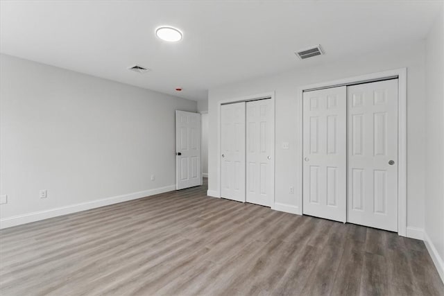 unfurnished bedroom with baseboards, wood finished floors, visible vents, and multiple closets