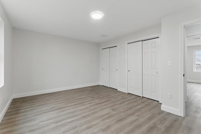 unfurnished bedroom with light wood finished floors, baseboards, and two closets