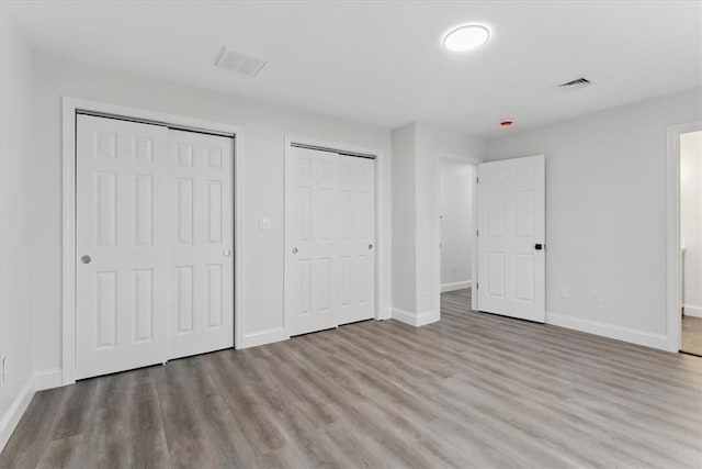 unfurnished bedroom with baseboards, wood finished floors, visible vents, and multiple closets