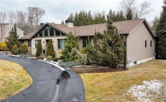 view of front of home featuring a shingled roof, stone siding, a chimney, and a front lawn