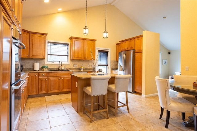 kitchen featuring light tile patterned floors, stainless steel appliances, a sink, brown cabinetry, and a center island with sink