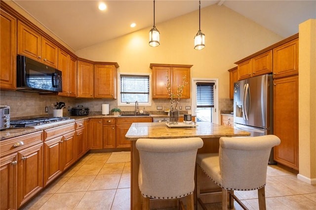 kitchen featuring light tile patterned floors, stainless steel appliances, brown cabinetry, a sink, and a kitchen island