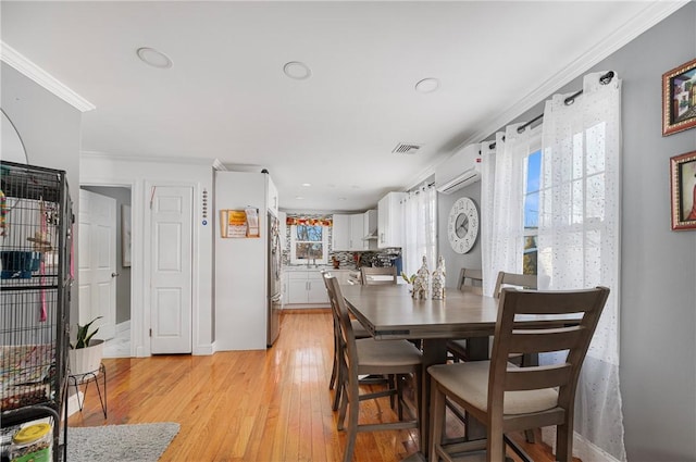 dining area with light wood-style flooring, visible vents, crown molding, and an AC wall unit