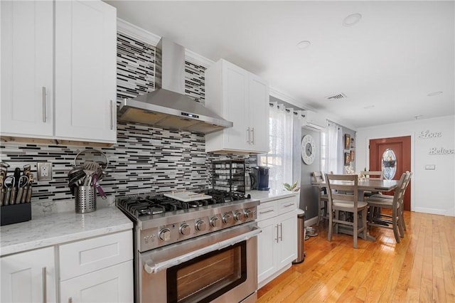 kitchen featuring wall chimney range hood, stainless steel range, plenty of natural light, and tasteful backsplash