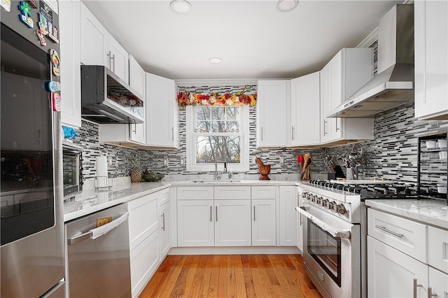 kitchen featuring wall chimney range hood, white cabinetry, stainless steel appliances, and light wood-style floors