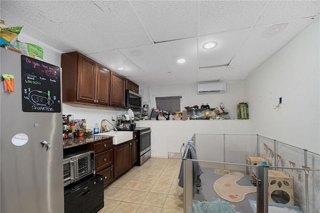 kitchen featuring stainless steel appliances, a paneled ceiling, a wall mounted AC, light tile patterned flooring, and a sink