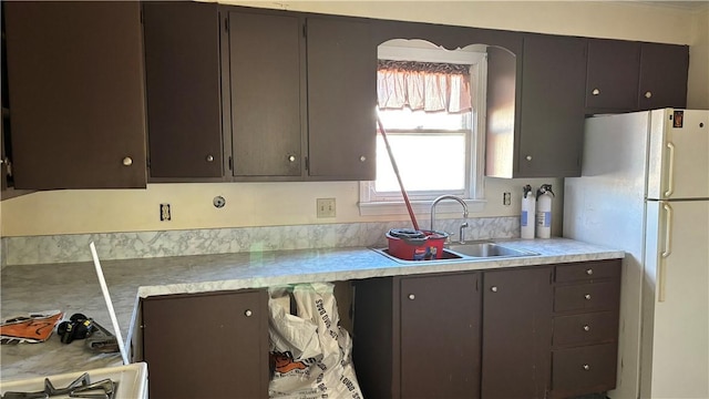 kitchen with arched walkways, light countertops, freestanding refrigerator, a sink, and dark brown cabinets