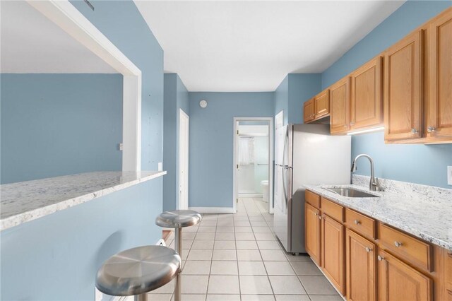 kitchen with light tile patterned floors, a sink, baseboards, freestanding refrigerator, and light stone countertops