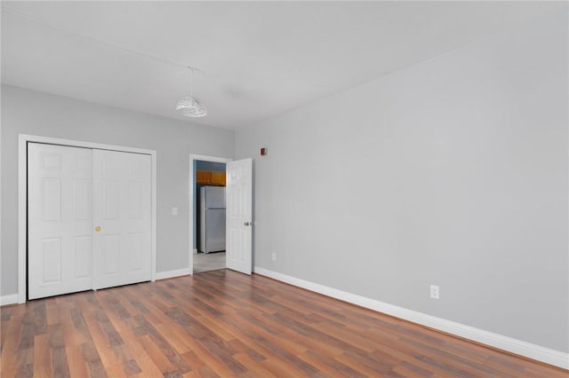 unfurnished bedroom featuring a closet, baseboards, wood finished floors, and freestanding refrigerator