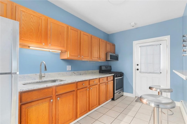 kitchen with appliances with stainless steel finishes, brown cabinets, light stone countertops, a sink, and light tile patterned flooring