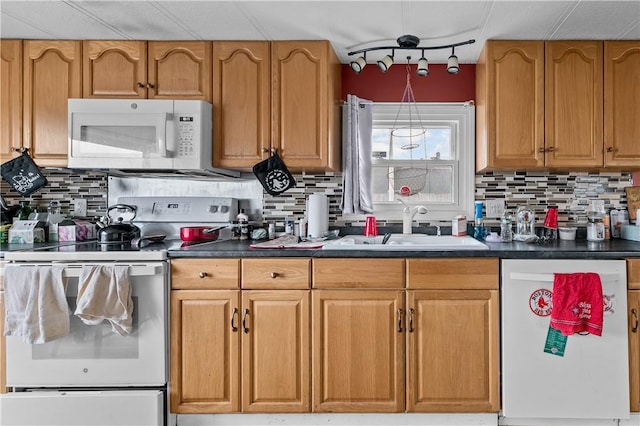 kitchen with white appliances, dark countertops, a sink, and tasteful backsplash