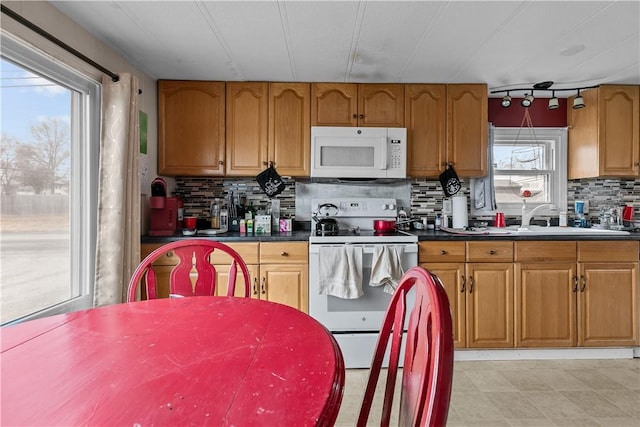 kitchen with brown cabinets, tasteful backsplash, dark countertops, a sink, and white appliances