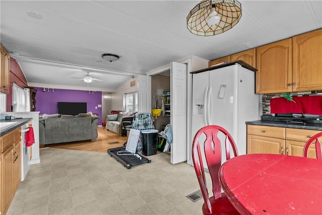 kitchen featuring white refrigerator with ice dispenser, dark countertops, lofted ceiling, ceiling fan, and light floors