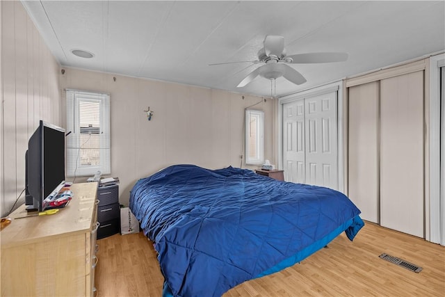 bedroom with ceiling fan, light wood finished floors, two closets, and visible vents