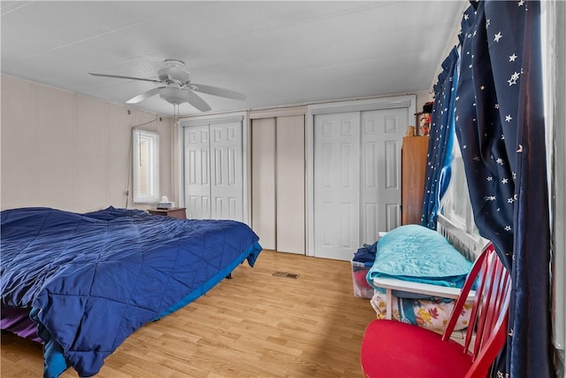 bedroom featuring ceiling fan, wood finished floors, visible vents, and multiple closets