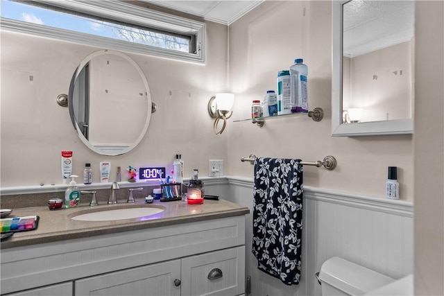 half bathroom with ornamental molding, a wainscoted wall, vanity, and toilet