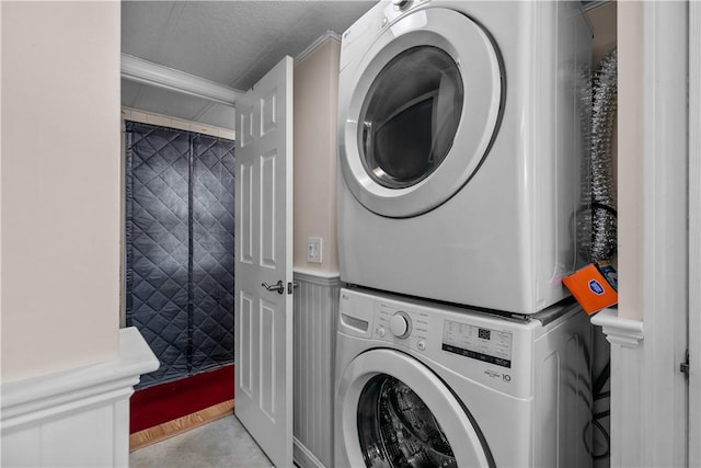 washroom featuring laundry area, a wainscoted wall, a decorative wall, and stacked washing maching and dryer