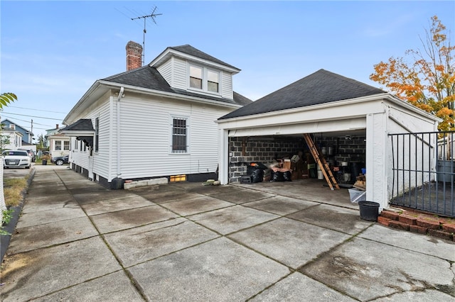 view of side of property featuring a garage, roof with shingles, an outdoor structure, and a chimney