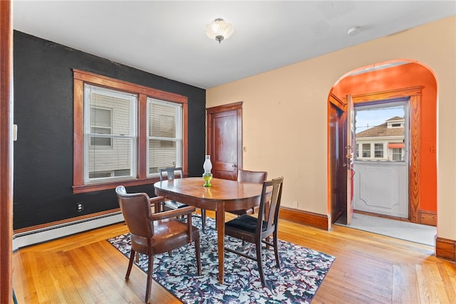 dining room with arched walkways, light wood finished floors, a baseboard radiator, and baseboards