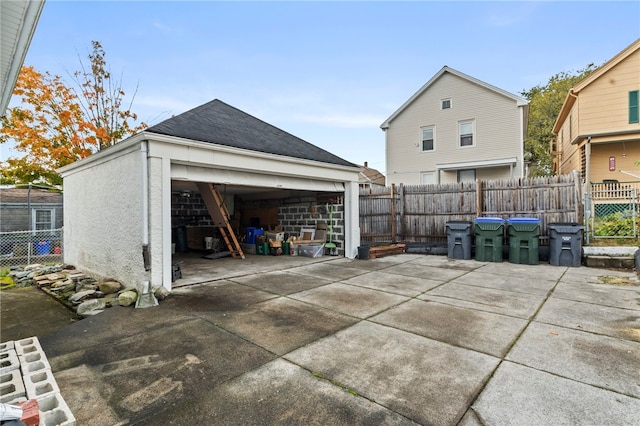 exterior space with a garage, an outbuilding, roof with shingles, and fence