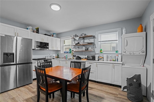 kitchen with stainless steel appliances, light wood-style flooring, stacked washing maching and dryer, and white cabinetry