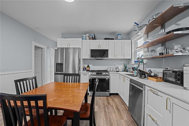 kitchen with light wood finished floors, wainscoting, appliances with stainless steel finishes, white cabinetry, and a sink