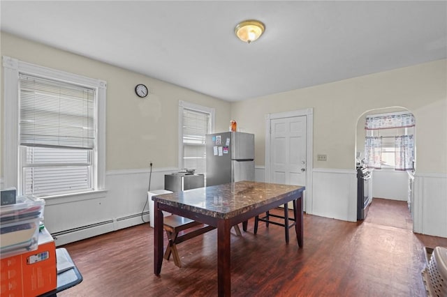 dining space with a wainscoted wall, arched walkways, baseboard heating, and wood finished floors