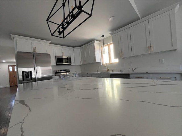 kitchen featuring light stone counters, stainless steel appliances, a sink, white cabinets, and decorative light fixtures