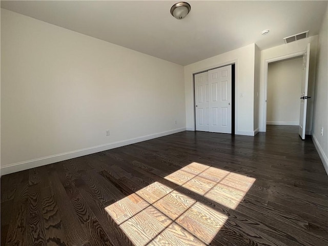 unfurnished bedroom with baseboards, a closet, visible vents, and dark wood-type flooring