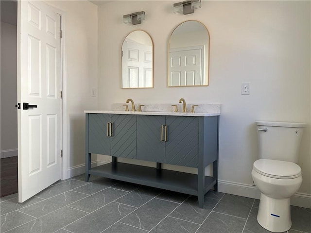 bathroom with double vanity, baseboards, toilet, marble finish floor, and a sink