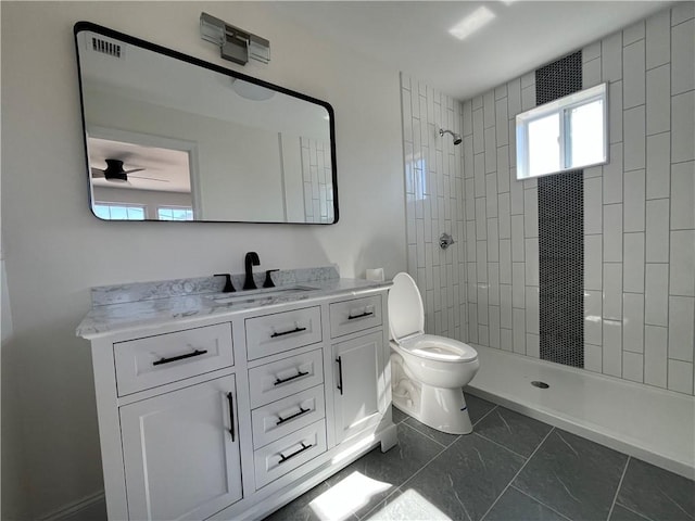 bathroom featuring toilet, ceiling fan, a tile shower, and vanity