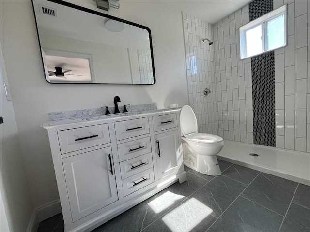 bathroom with toilet, visible vents, vanity, baseboards, and a tile shower