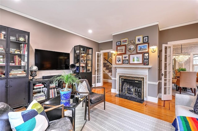 living room featuring wood finished floors, a fireplace with flush hearth, baseboards, ornamental molding, and french doors