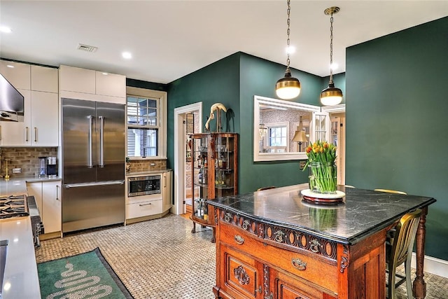 kitchen featuring built in appliances, visible vents, white cabinets, hanging light fixtures, and decorative backsplash