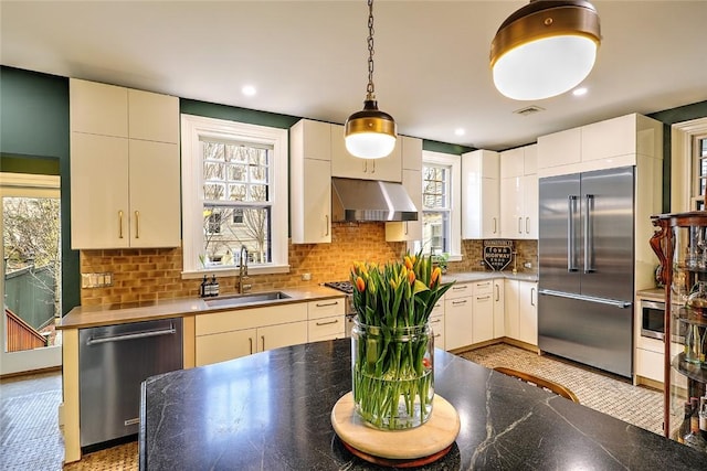 kitchen with tasteful backsplash, decorative light fixtures, built in appliances, under cabinet range hood, and a sink