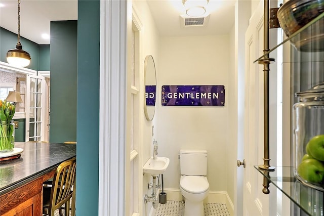 half bath with toilet, visible vents, and baseboards