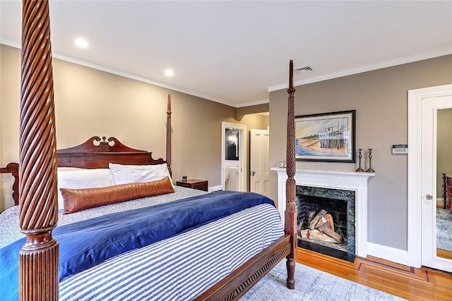 bedroom featuring a fireplace, wood finished floors, visible vents, baseboards, and crown molding