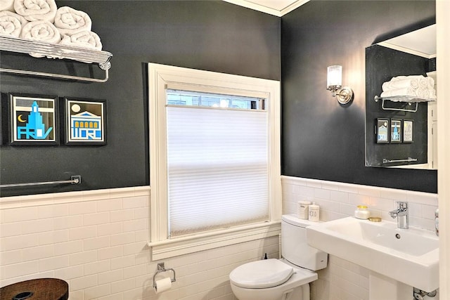 bathroom with a sink, toilet, tile walls, and wainscoting