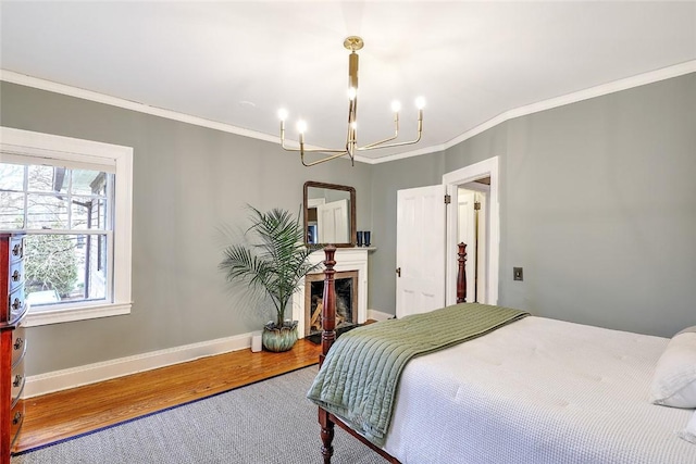 bedroom featuring baseboards, ornamental molding, wood finished floors, a fireplace, and a chandelier