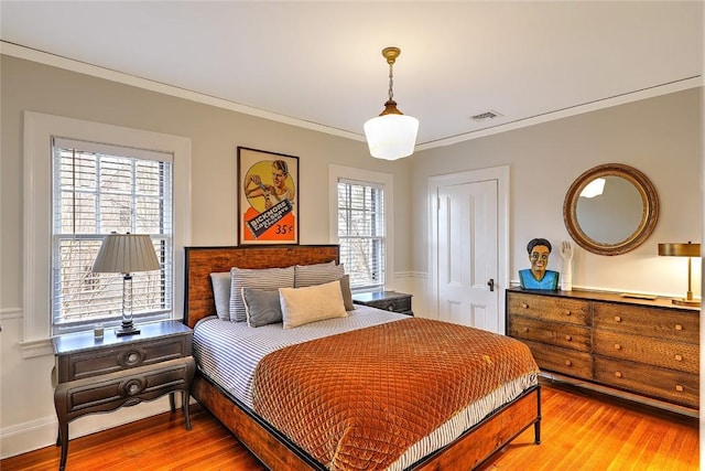 bedroom with ornamental molding, visible vents, baseboards, and wood finished floors