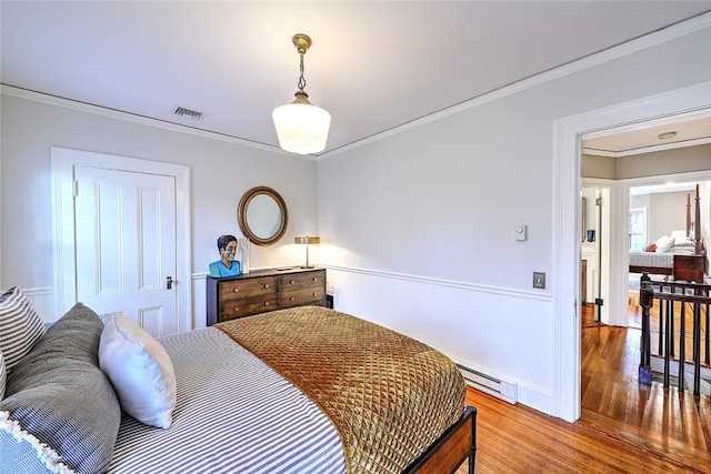 bedroom with baseboards, ornamental molding, baseboard heating, and wood finished floors