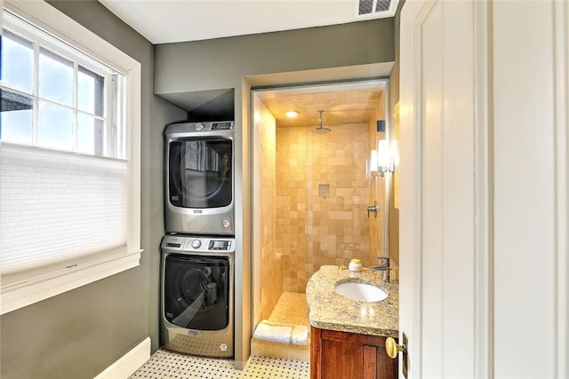 laundry area featuring stacked washer and clothes dryer, visible vents, a sink, laundry area, and baseboards