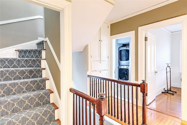 staircase with ornamental molding, stacked washer / drying machine, and wood finished floors