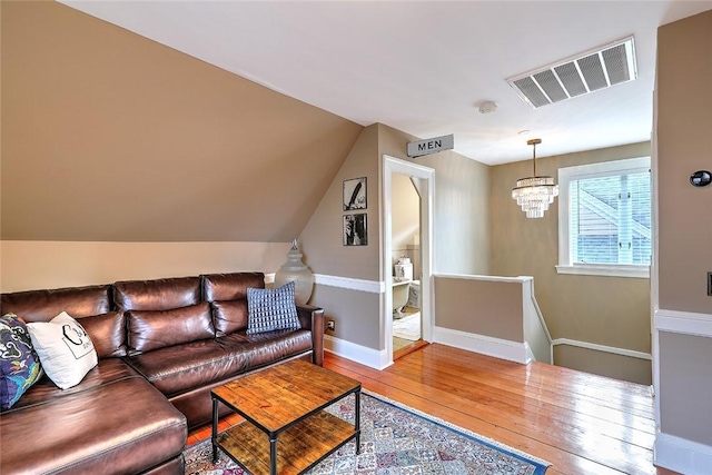 living area with lofted ceiling, a notable chandelier, visible vents, baseboards, and wood-type flooring