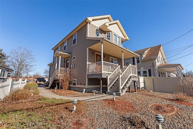 view of front of house featuring covered porch, stairway, and fence