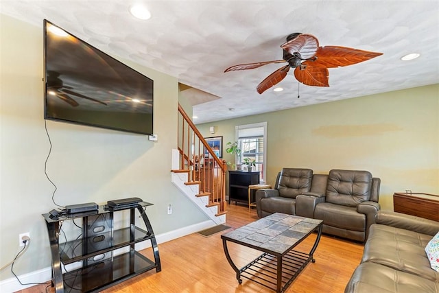 living area featuring stairs, ceiling fan, baseboards, and light wood-style floors