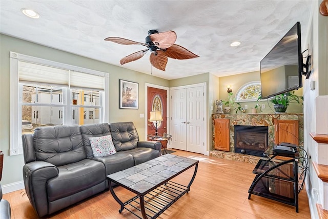 living room featuring a high end fireplace, baseboards, ceiling fan, and light wood finished floors