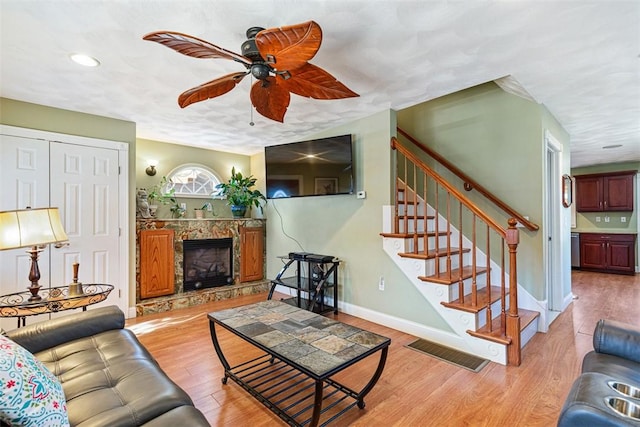 living room featuring a fireplace, light wood finished floors, visible vents, baseboards, and stairs