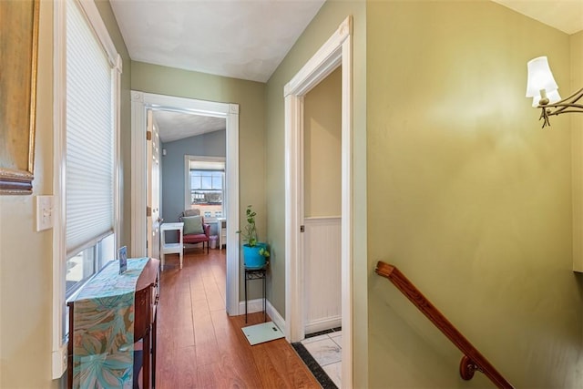 hall with baseboards, a chandelier, wood finished floors, and an upstairs landing