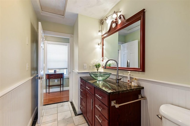 half bathroom with toilet, tile patterned floors, vanity, and wainscoting